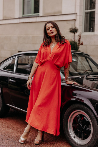 Femme avec une robe corail sur une voiture.