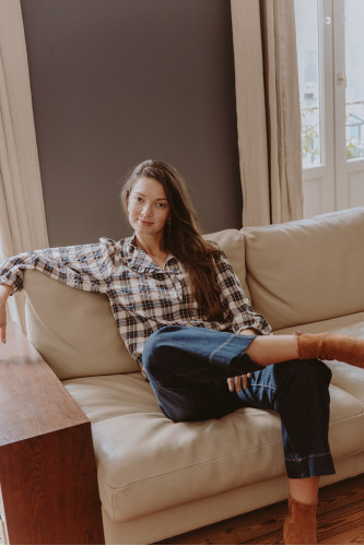 Femme assise dans un canapé avec une blouse à carreaux.