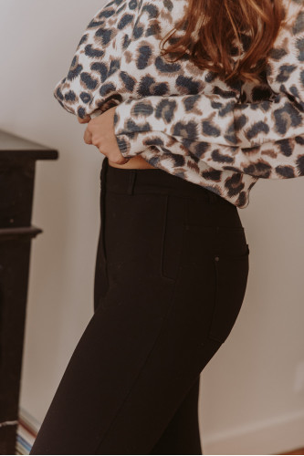 Femme qui porte un pantalon noir et un pull léopard.